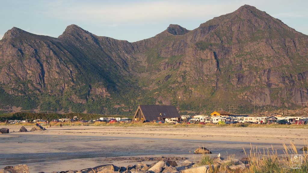 The evening sun casts a soft glow on a beachside camping area, a more adventurous choice for where to stay in Lofoten with magnificent mountain views in the background.