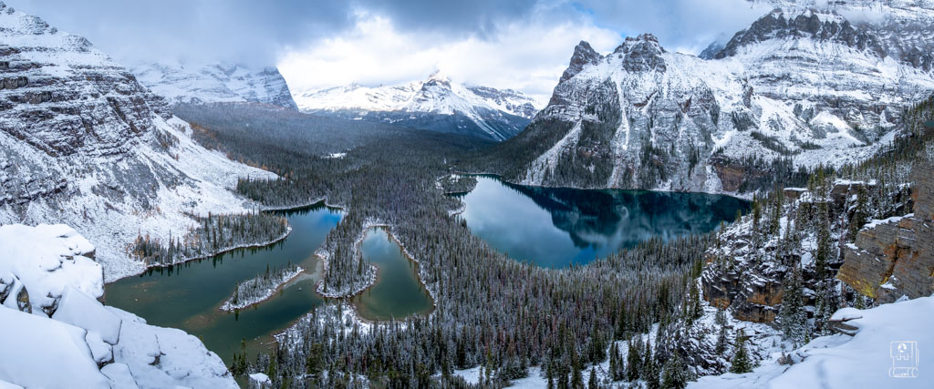 Panoramic winter view of Lake O'Hara hiking trails and surrounding peaks in Yoho National Park, featuring snow-covered mountains and turquoise alpine lakes reflecting the Canadian Rockies landscape