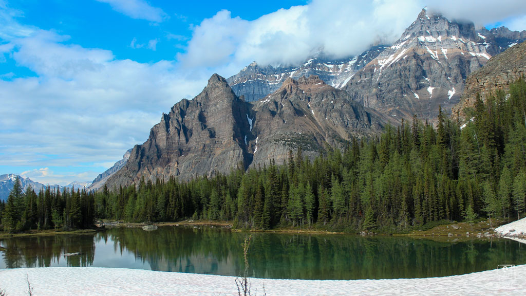 Pristine alpine lake reflecting jagged mountain peaks and evergreen forest, showcasing the stunning landscapes on the Lake O'Hara hiking itinerary